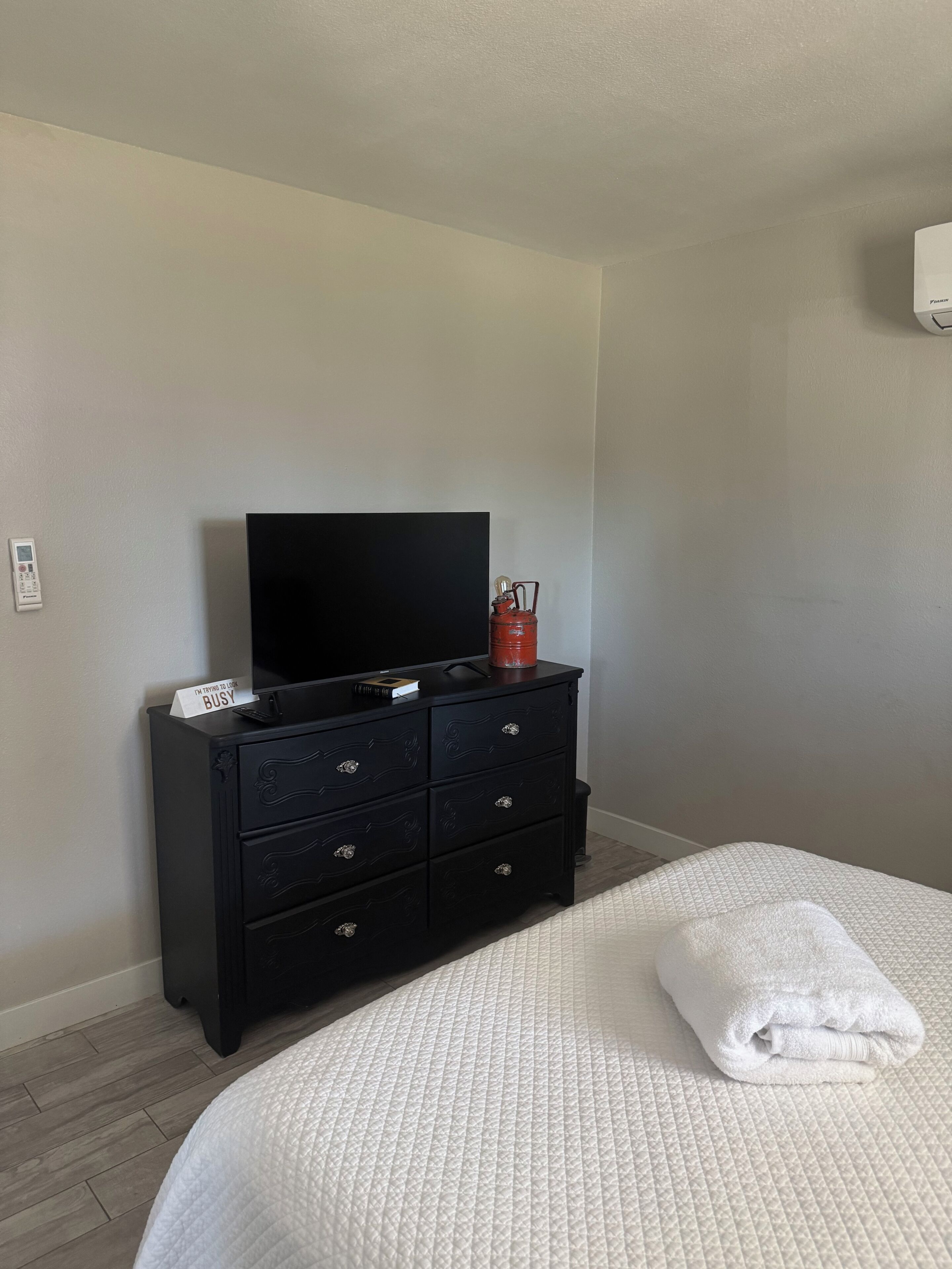 Un dormitorio con una cama, un aparador negro con un televisor de pantalla plana, una vela roja y un cartel en el aparador.