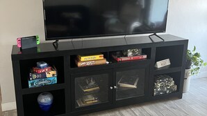 Un meuble de rangement noir pour appareils multimédias, avec un téléviseur à écran plat, des livres et des jeux de société.