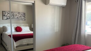 Une chambre à coucher comprenant un lit, un miroir, un climatiseur fixé au mur et une fenêtre avec des rideaux.
