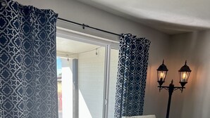 Deux fauteuils inclinables dans une pièce dotée d’un plancher en bois, d’une fenêtre ornée de rideaux à motifs et d’une lampe fixée au mur.