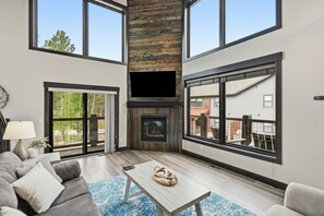 A modern living room with a fireplace, large windows, and a view of the outside.