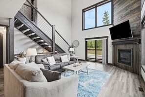 Una sala de estar moderna con una escalera, una chimenea y un ventanal grande.