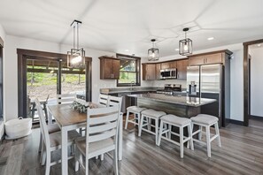 Una cocina moderna con una isla central, electrodomésticos de acero inoxidable y una zona de comedor con sillas blancas.