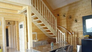 A wooden interior with a dining table, chairs, a staircase, and a television.