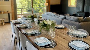 Un coin repas avec une longue table en bois dressée pour le repas, un canapé gris et une cheminée.
