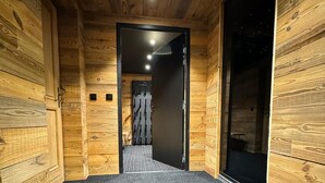 Un couloir aux murs en bois et au sol recouvert d’une moquette, qui mène à une pièce dotée d’une porte noire et offrant une vue sur un ciel étoilé.