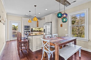 Una cocina con armarios blancos, un refrigerador de acero inoxidable y una zona de comedor con una mesa de madera y sillas blancas.