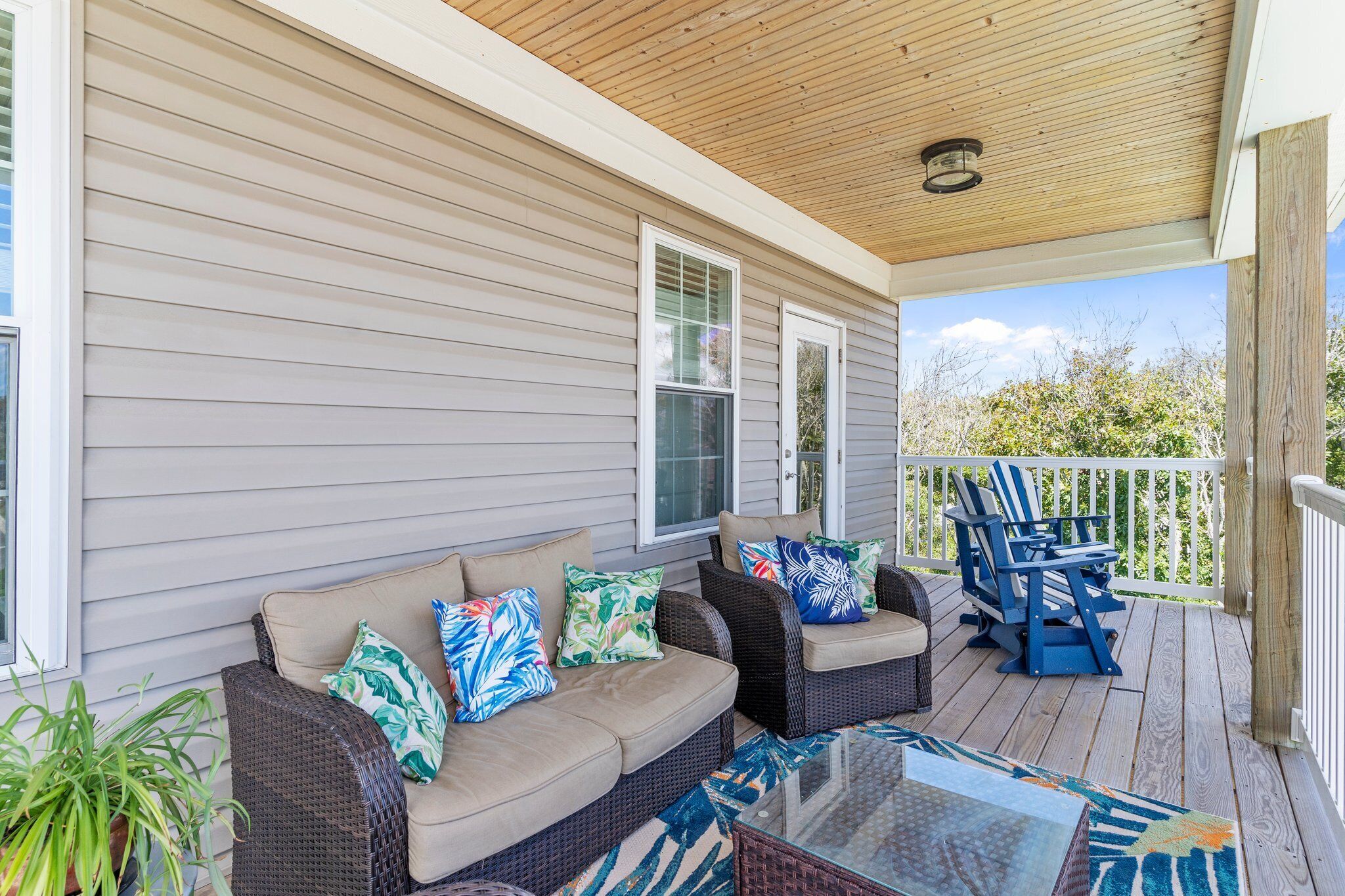 A covered porch with wicker furniture and a glass table.