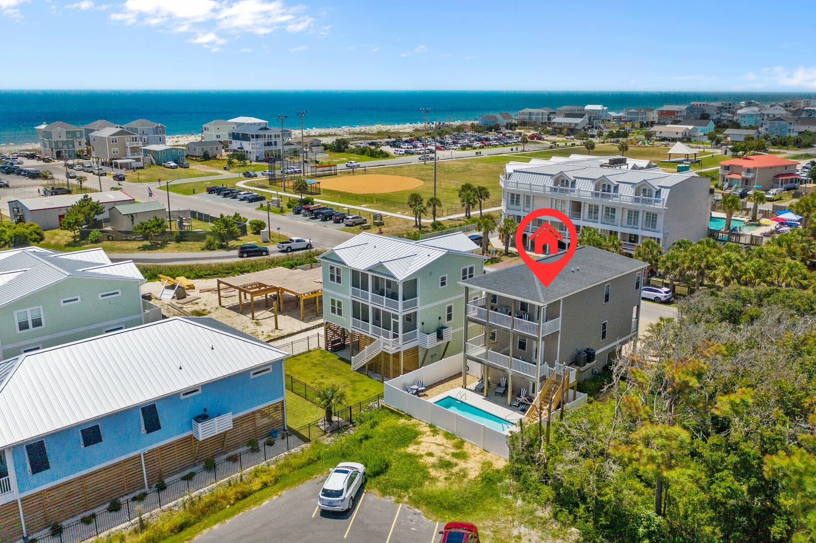 A residential area with a large building featuring a pool, a baseball field, and a view of the ocean.