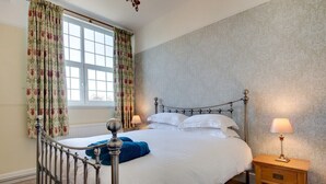 A neatly made bed with white linens, a metal headboard, and a wooden nightstand with a lamp.