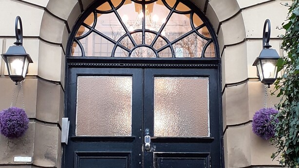 A black double door with a glass panel, a small sign, and two lantern-style lights.
