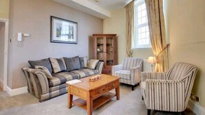 A living room with a sofa, a wooden coffee table, striped armchairs, a cabinet, and a framed picture on the wall.