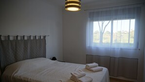 A neatly made bed with a quilted headboard, a window with sheer curtains, and a hanging light fixture. - Quiet F4 apartment 5 minutes from Olhão town center, Algarve  (QUELFES)
