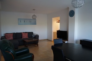 Un salon comprenant un canapé, une table basse et des fauteuils, une table à manger, un téléviseur et un tableau accroché au mur.