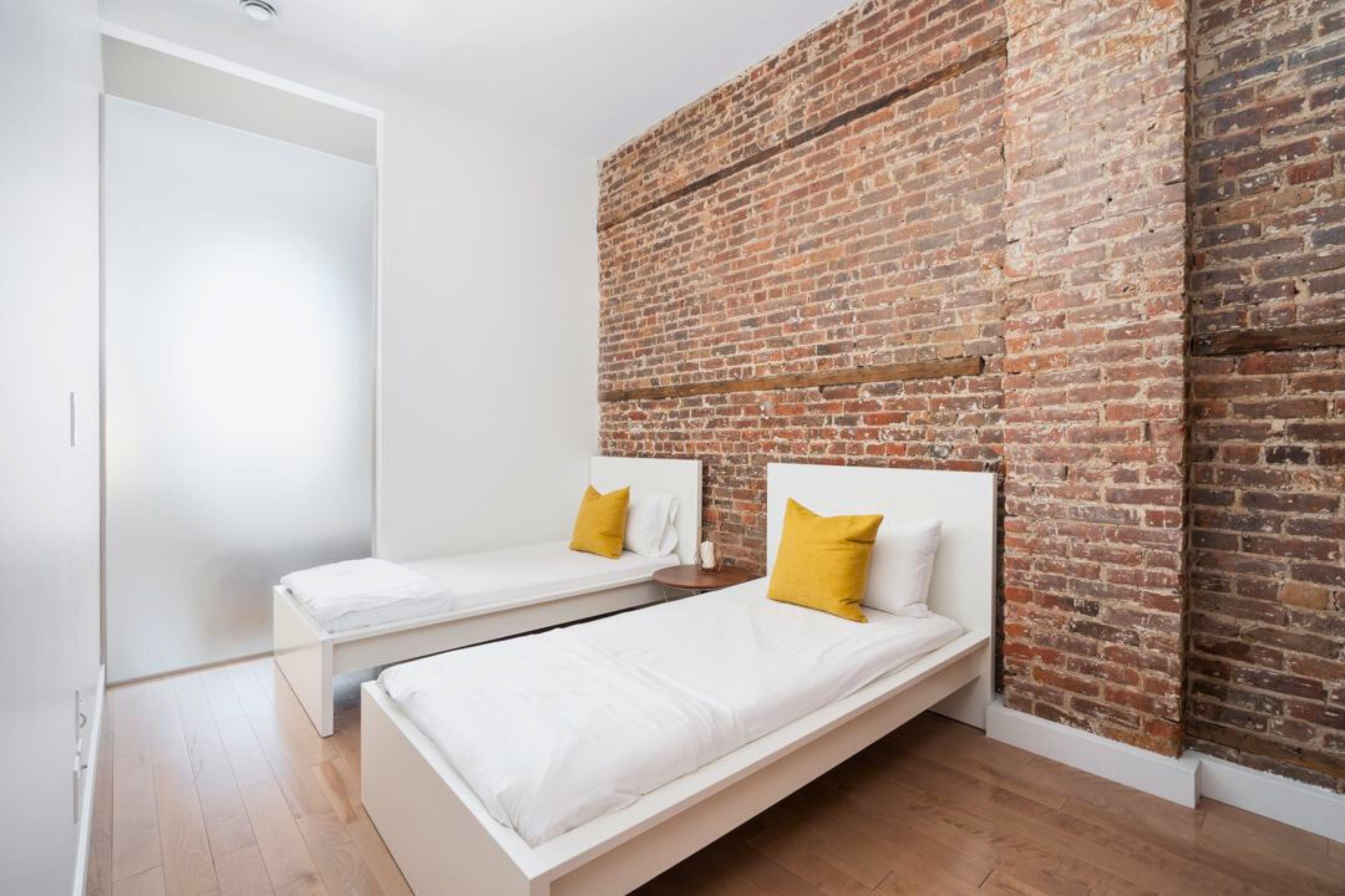 Un dormitorio con dos camas individuales, ropa de cama blanca y almohadas amarillas.