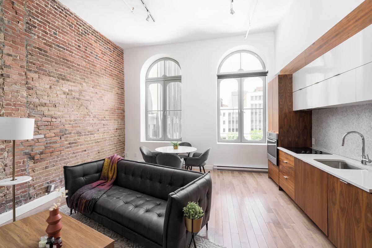 A modern kitchen with a brick wall, a black leather sofa, and a dining area with a round table and chairs.