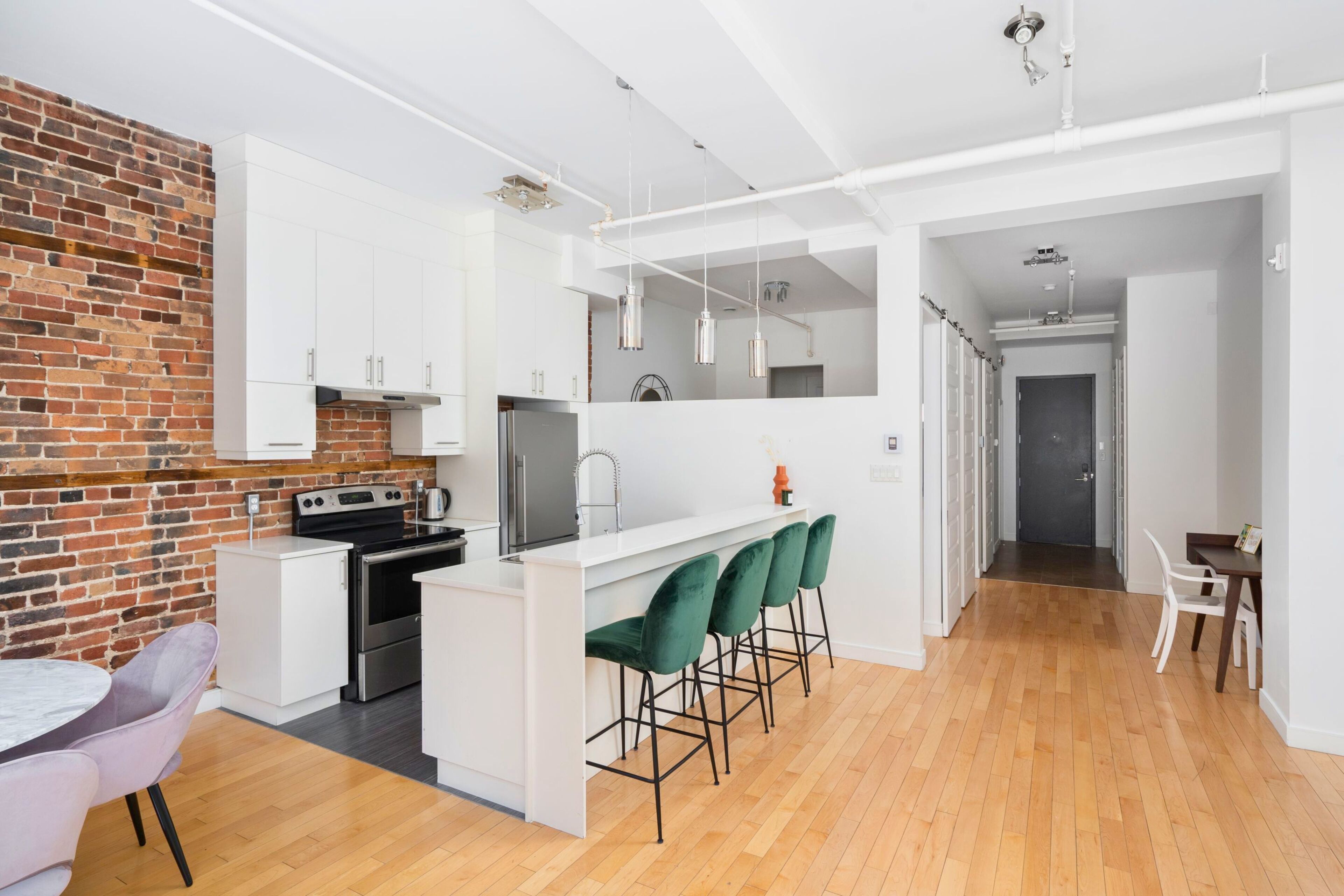 Cocina moderna con armarios blancos, una pared de ladrillo decorativa y una isla central con taburetes de bar.