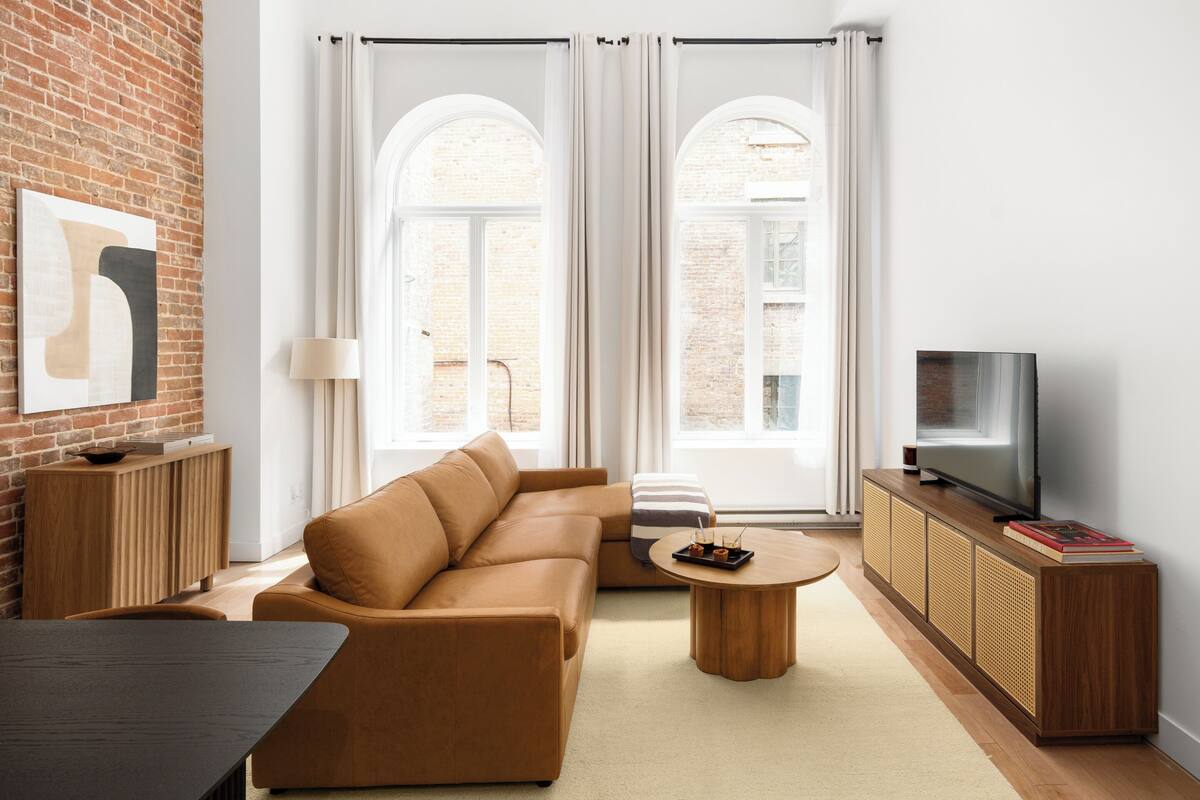 A modern living room with a sofa, coffee table, TV, and a brick wall.