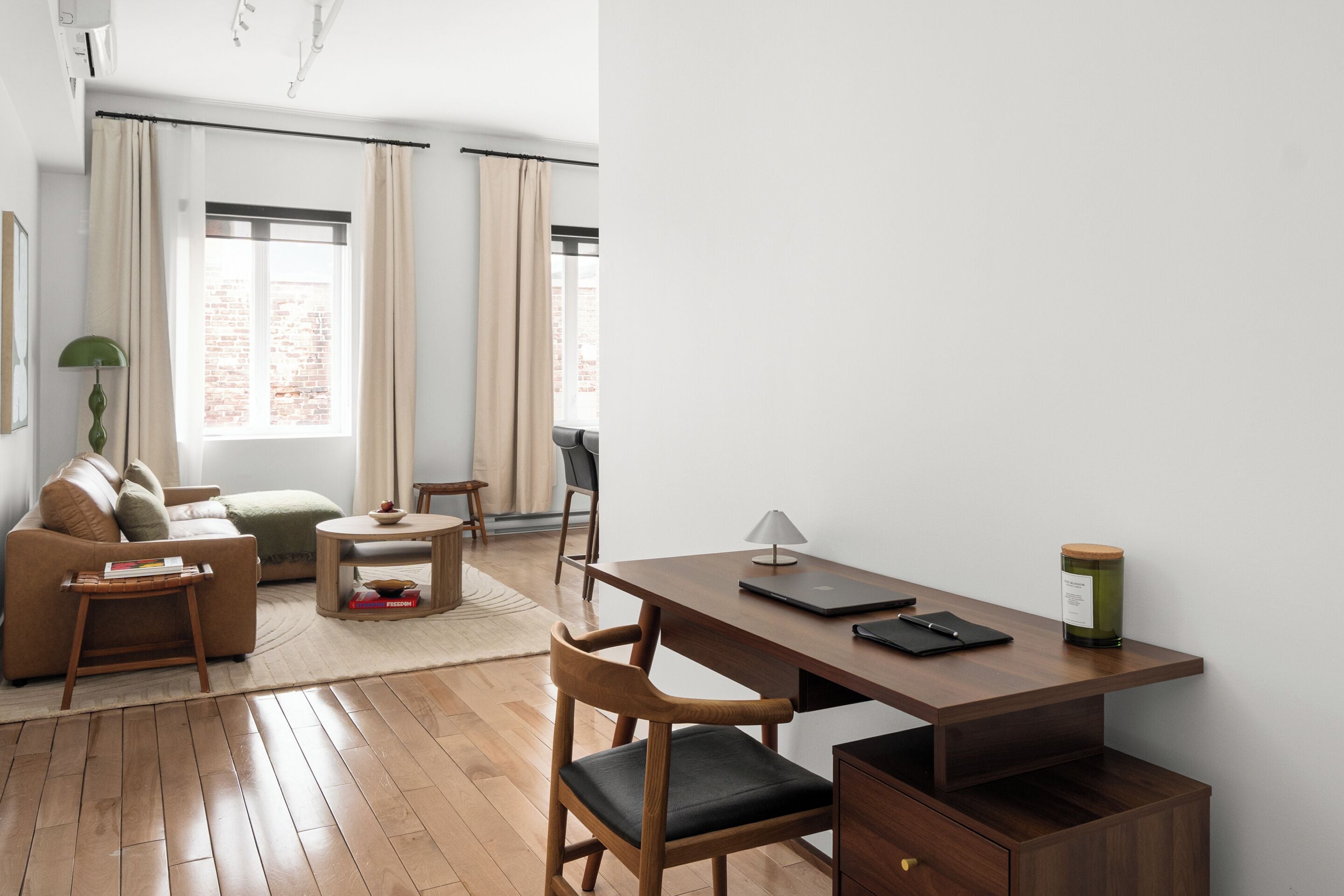 A modern living room with a wooden desk, a sofa, and a dining area.