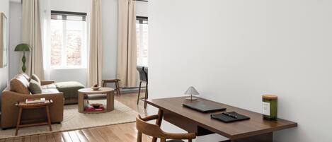A modern living room with a wooden desk, a sofa, and a dining area.