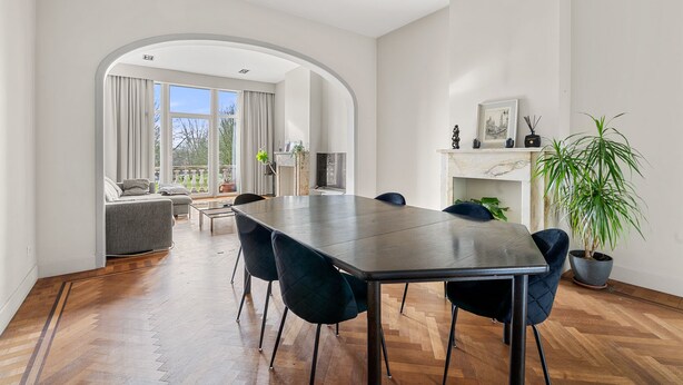 Ein moderner Essbereich mit einem langen Tisch, Stühlen, einem Kamin und einem großen Fenster mit Vorhängen.