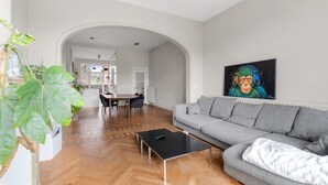 Ein geräumiges Wohnzimmer mit einem grauen Sofa, einem schwarzen Couchtisch und einer großen Pflanze.
