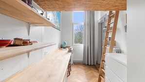 Eine Küche mit Holzregalen, einem Fischgrätparkett, einem Fenster mit Vorhängen und einer an der Wand stehenden Leiter.