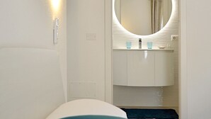 A hotel room with a bed, a round mirror above the sink, and a wall-mounted light.