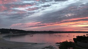 Un coucher de soleil sur la côte, avec des bateaux sur l’eau et une plage au premier plan.