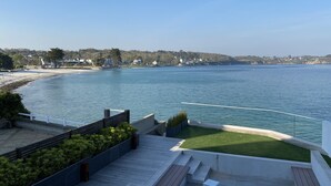 Une terrasse extérieure moderne offrant une vue sur une mer calme et une côte lointaine parsemée de maisons.