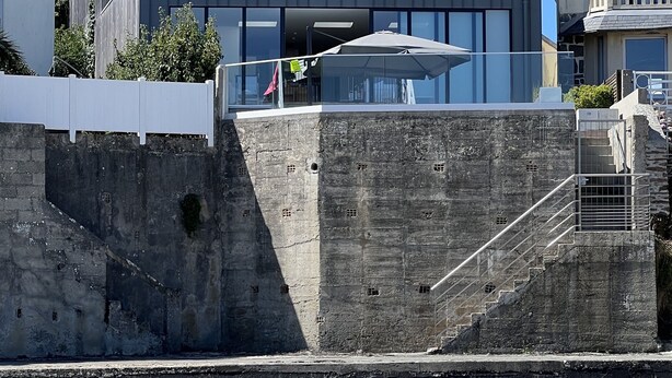 Une maison moderne à deux étages, dotée d’un balcon, d’un mur en pierre et d’un escalier menant à l’entrée.