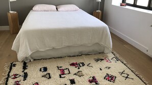 Une chambre à coucher avec un lit, deux lampes de chevet, une fenêtre et un tapis à motifs.