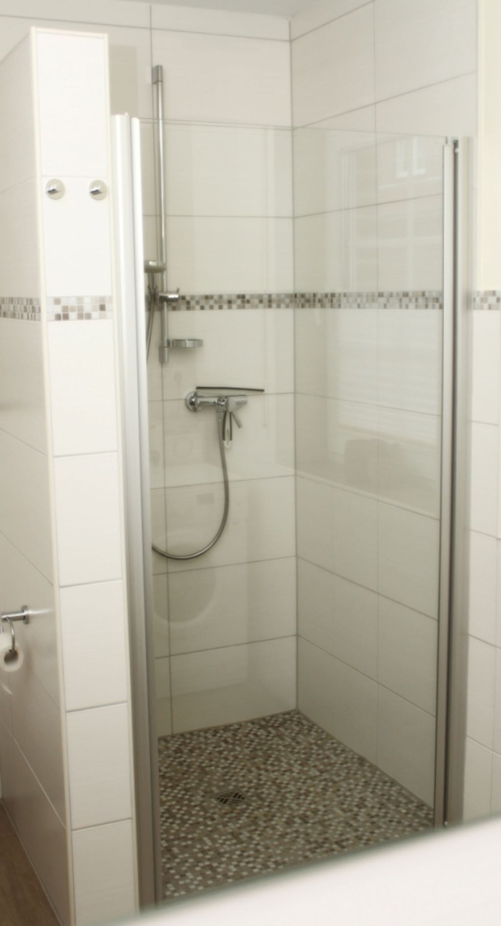 A glass-enclosed shower stall with a tiled floor and a white wall with a decorative border.