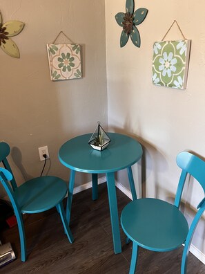 Een tafelset in teal staat voor een beige muur, versierd met decoratieve wandobjecten.