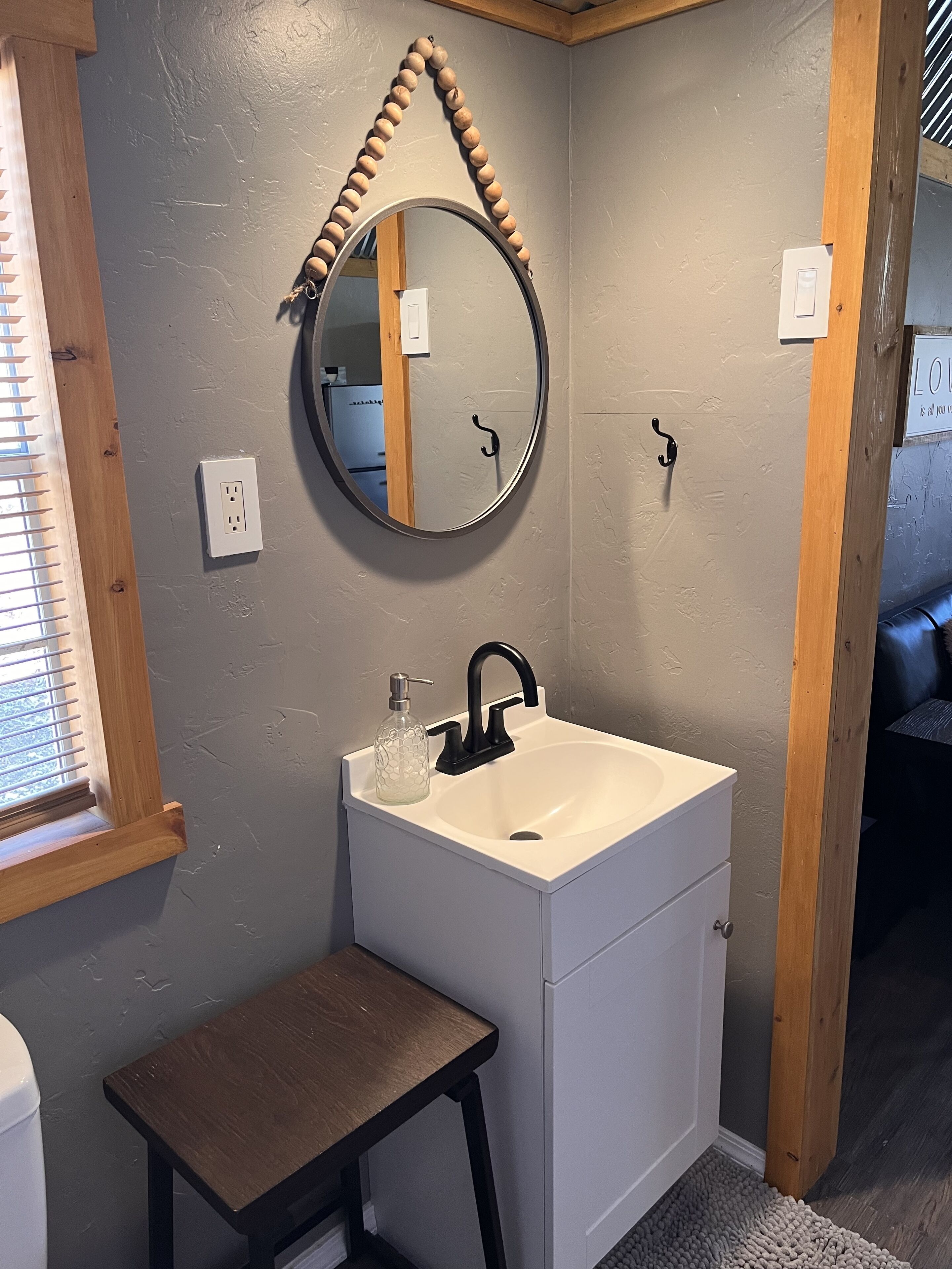 Un baño con un lavamanos blanco, grifo negro y un taburete de madera.