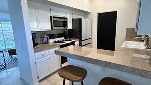 Uma cozinha moderna com armários brancos, bancada de granito, geladeira preta e dois banquetas de madeira.