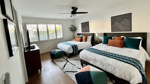 Quarto com duas camas, ventoinha no teto e janela com persianas.