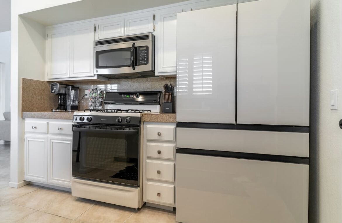 Una cucina con mobili bianchi, un forno a microonde in acciaio inox, un piano cottura a gas e un forno integrato.