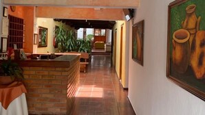 A hallway with a reception desk, potted plants, and framed artwork on the walls. - Hotel Sol De La Villa (Villa de Leyva)