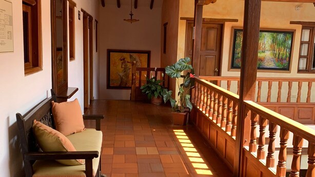 A covered corridor with a wooden bench, potted plants, and a painting on the wall. - Hotel Sol De La Villa (Villa de Leyva)
