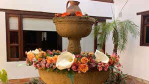A stone fountain with flowers and a palm tree in a courtyard. - Hotel Sol De La Villa (Villa de Leyva)