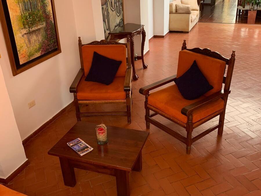 A spacious lobby with two wooden armchairs with cushions, a wooden coffee table, and a sofa.