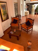 A spacious lobby with two wooden armchairs with cushions, a wooden coffee table, and a sofa.