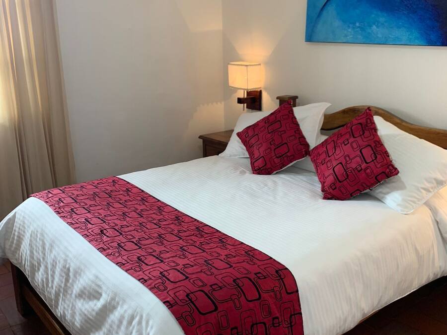 A hotel room with a bed, a nightstand with a lamp, a painting on the wall, and a window with curtains.