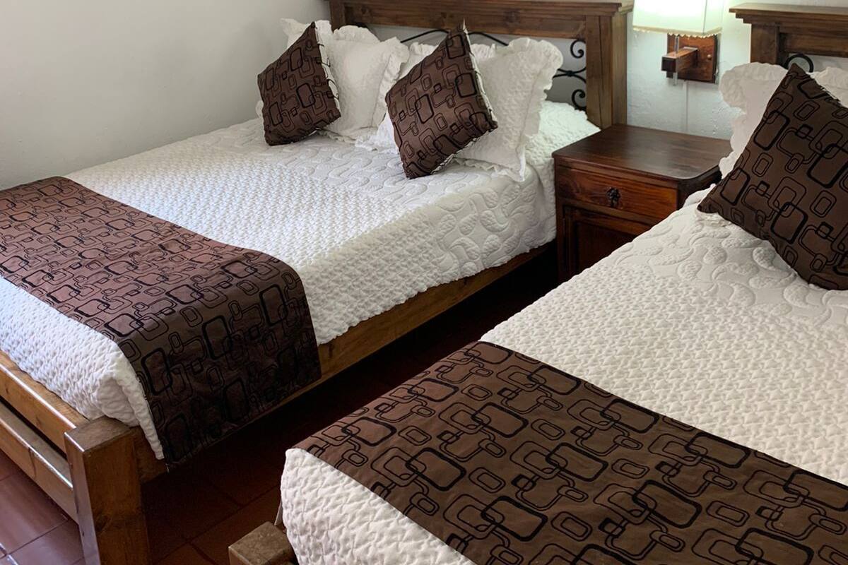 Quarto duplo com duas camas, cada uma com colcha e almofadas estampadas, cabeceira de madeira, mesa de cabeceira com abajur e uma obra de arte na parede.