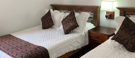 A double room with two beds, each with a patterned bedspread and pillows, a wooden headboard, a bedside table with a lamp, and a wall-mounted artwork.