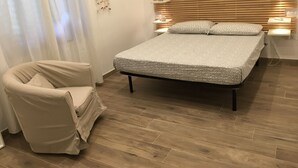 Ein Schlafzimmer mit einem Bett, einem Sessel, Holzboden und einer Wandleuchte.
