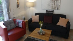 A living room with a red armchair, a black sofa, a wooden coffee table with a vase, and a painting on the wall.