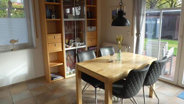 A dining area with a wooden table, black chairs, a bookshelf, and a hanging light fixture.