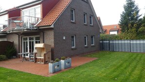 A two-story house with a red-tiled roof, a balcony, and a well-maintained lawn.